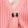 A close-up of a pink knitted sweater featuring a black and gold rhinestone brooch button.