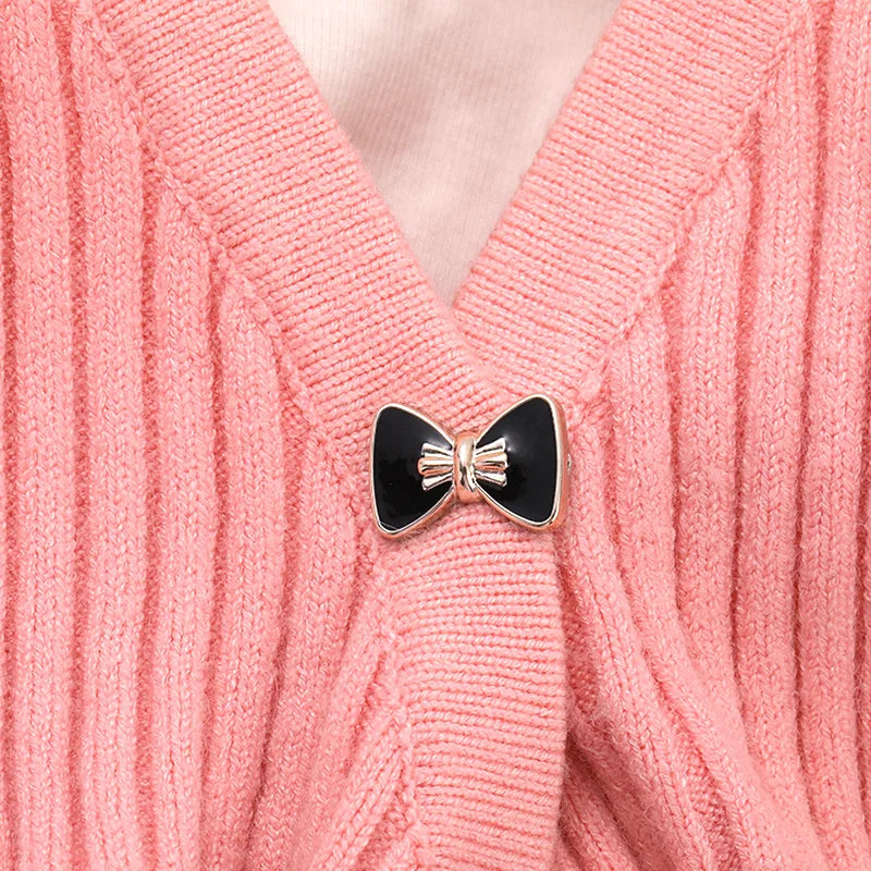 A close-up of a pink knitted sweater featuring a black and gold rhinestone brooch button.