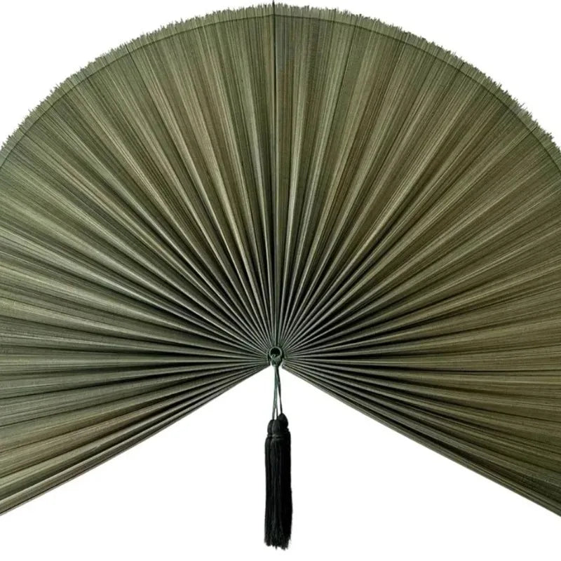 A handwoven bamboo wall fan decor with a wide, pleated fan and a black tassel.