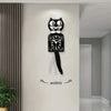 A black cartoon cat wall clock with a white bow and swinging tail mounted on a white wall.