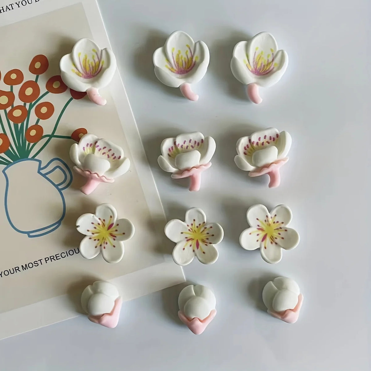 A set of twelve white and pink kawaii flower decorative fridge magnets arranged on a white background.