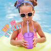 A young girl wearing pink swimwear and sunglasses is holding a purple reusable sipper cup outdoors.