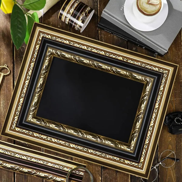 A framed black picture with a vintage gold decorative border, resting on a wooden surface.