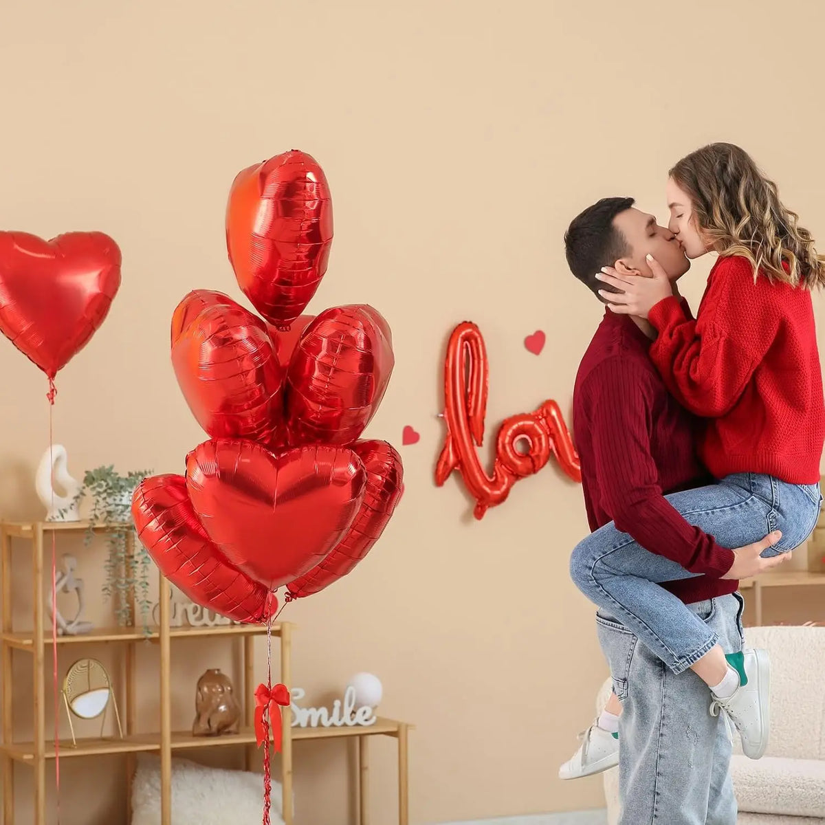 A couple is kissing in front of a wall decorated with red heart foil balloons.