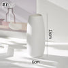 A white ceramic bud vase with a smooth, elongated shape is shown on a light surface.