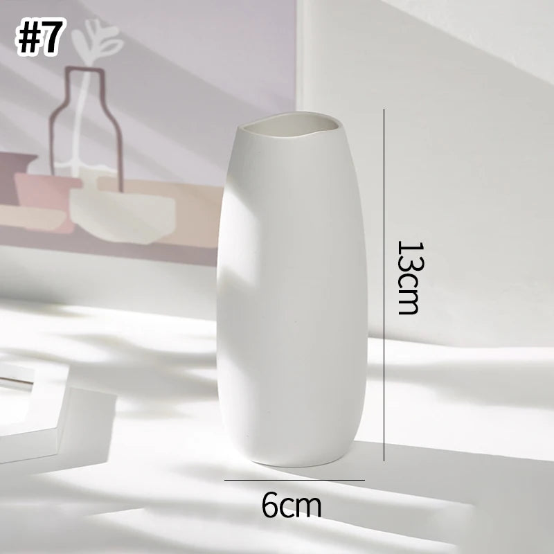 A white ceramic bud vase with a smooth, elongated shape is shown on a light surface.