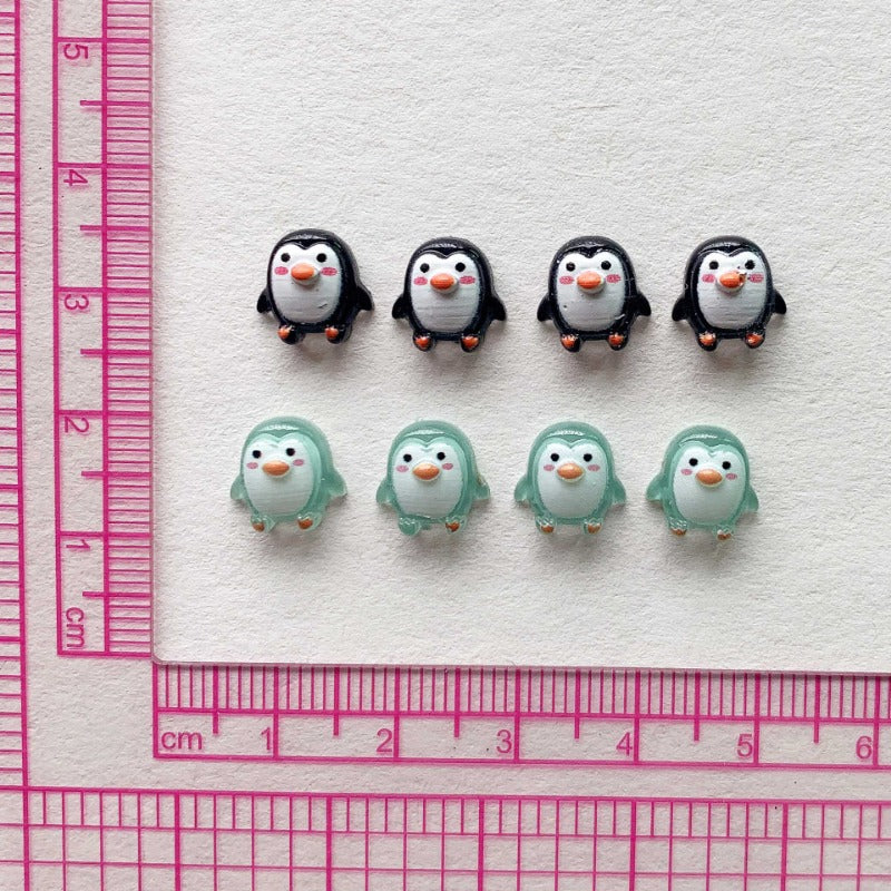 A set of 12 resin mini penguin figurines arranged on a white background next to a ruler.