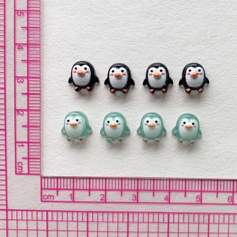A collection of black and white resin mini penguin figurines arranged on a white background next to a ruler.