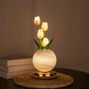 A vase holds three glowing yellow tulips, illuminated by a warm light, resting on a woven mat.