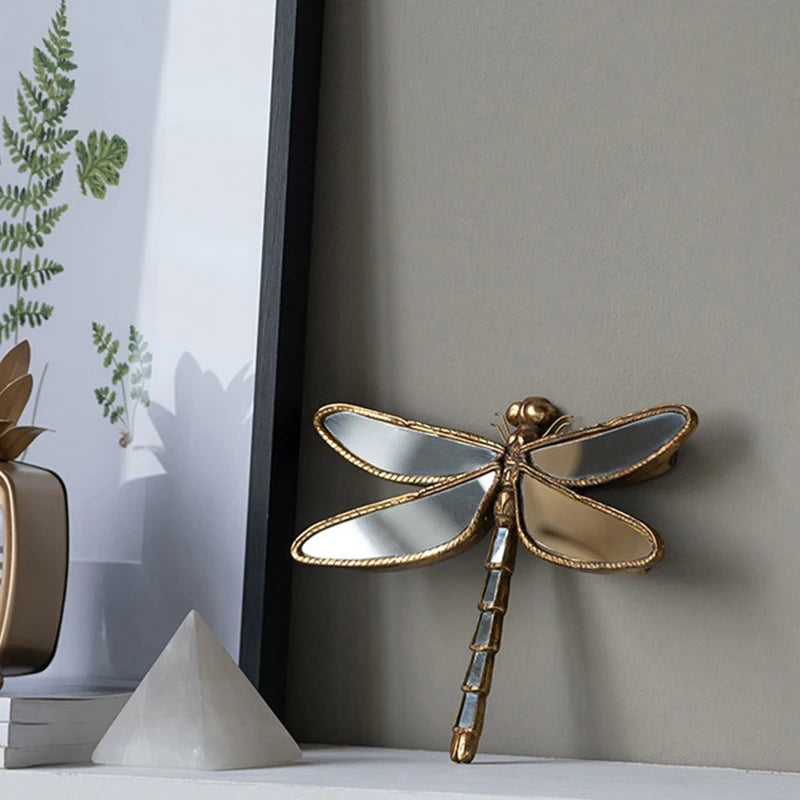 An artisan butterfly wall mirror with an antique gold frame mounted on a gray wall.