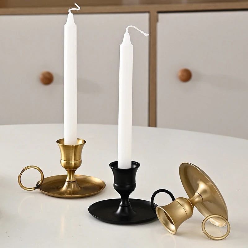 A set of elegant brass and black metal candle holders with handles displayed on a white table.