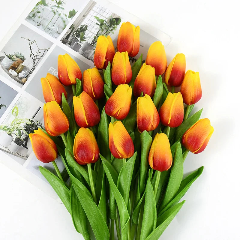 A bouquet of lifelike artificial orange and yellow tulips with green stems and leaves.