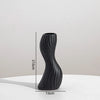 A black, textured ceramic vase with an elongated, curved shape is shown against a white background.