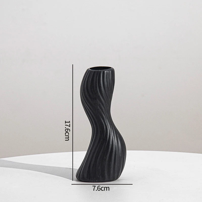 A black, textured ceramic vase with an elongated, curved shape is shown against a white background.