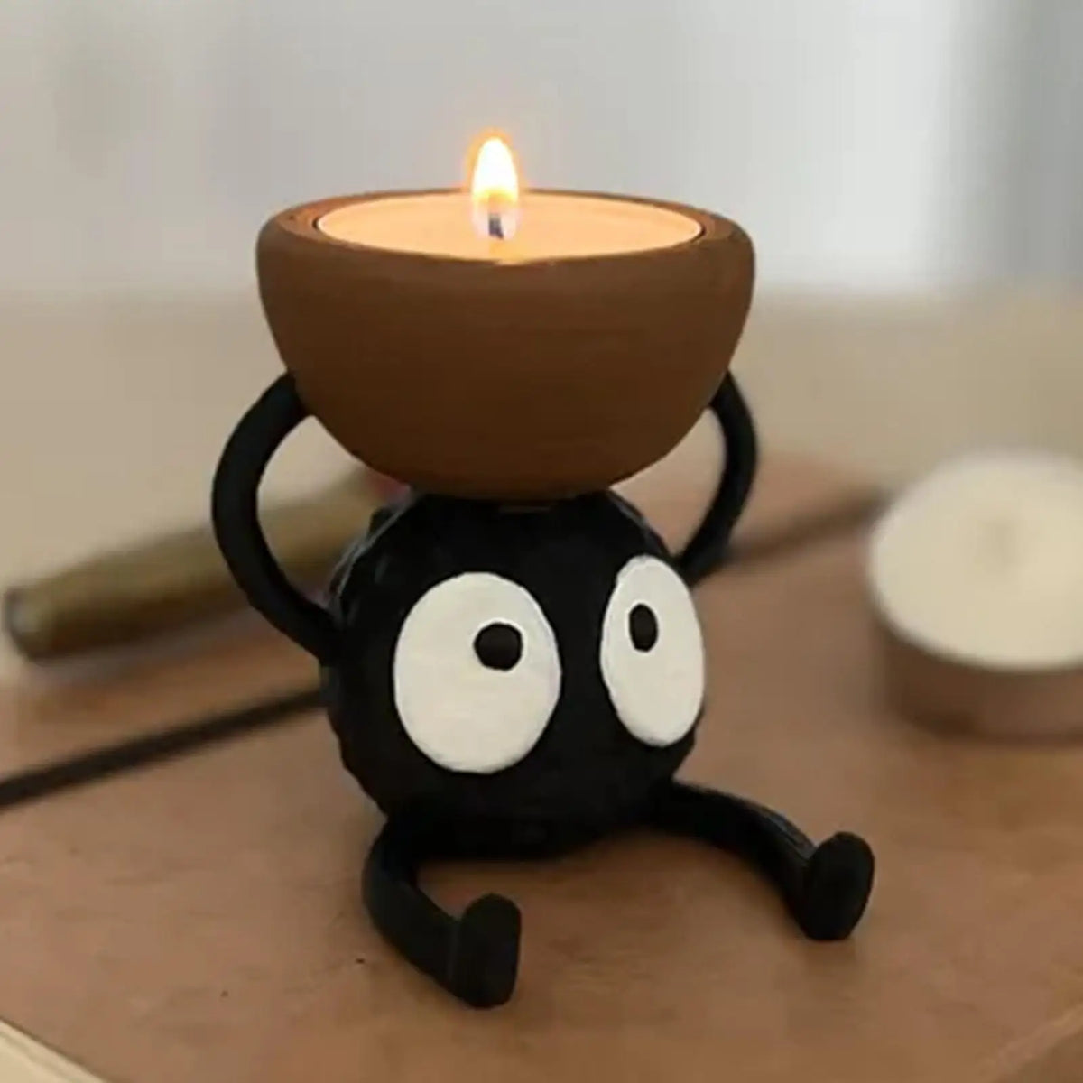 Schwarzer 3D-gedruckter Kerzenständer in Form eines Cartoon-Auges, der eine brennende Kerze hält.