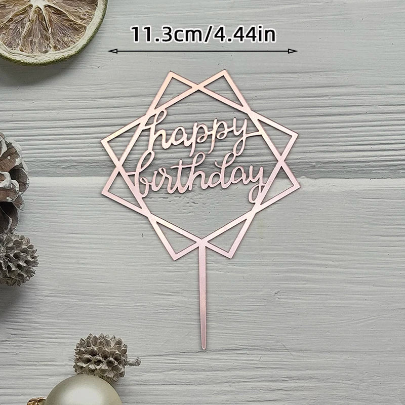 A pink acrylic birthday sign with a geometric shape and text on a wooden surface surrounded by pinecones.