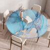 A round table set for dining featuring a marble print tablecloth with blue and pink tones and gold accents.