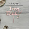 A rose gold acrylic cake topper set spelling out Happy Birthday on a wooden surface.