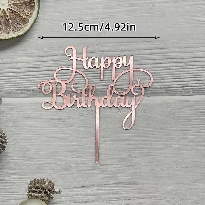 A rose gold acrylic cake topper set spelling out Happy Birthday on a wooden surface.