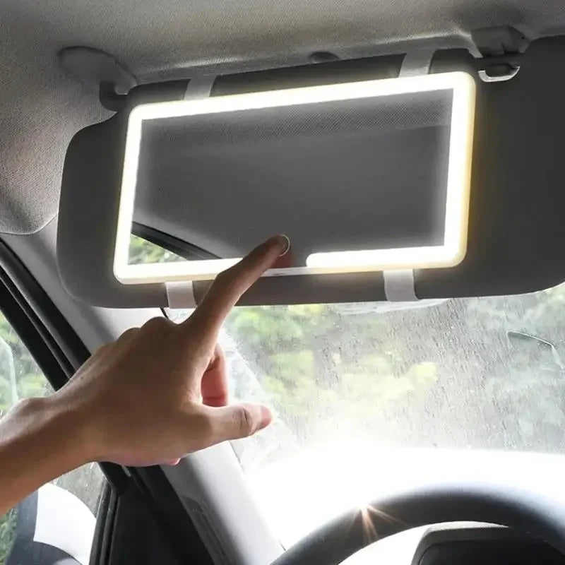 A hand is adjusting an LED car sun visor vanity mirror with adjustable straps inside a vehicle.