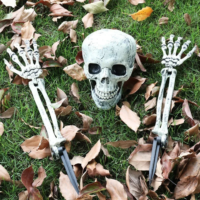 A realistic white skeleton hand lawn stake is shown lying on green grass amidst fallen autumn leaves.