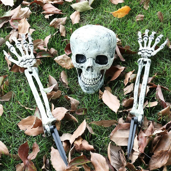 A realistic white skeleton hand lawn stake is shown lying on green grass amidst fallen autumn leaves.