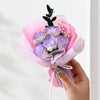 A hand holds a bouquet of handcrafted soap roses wrapped in pink and purple tissue paper.