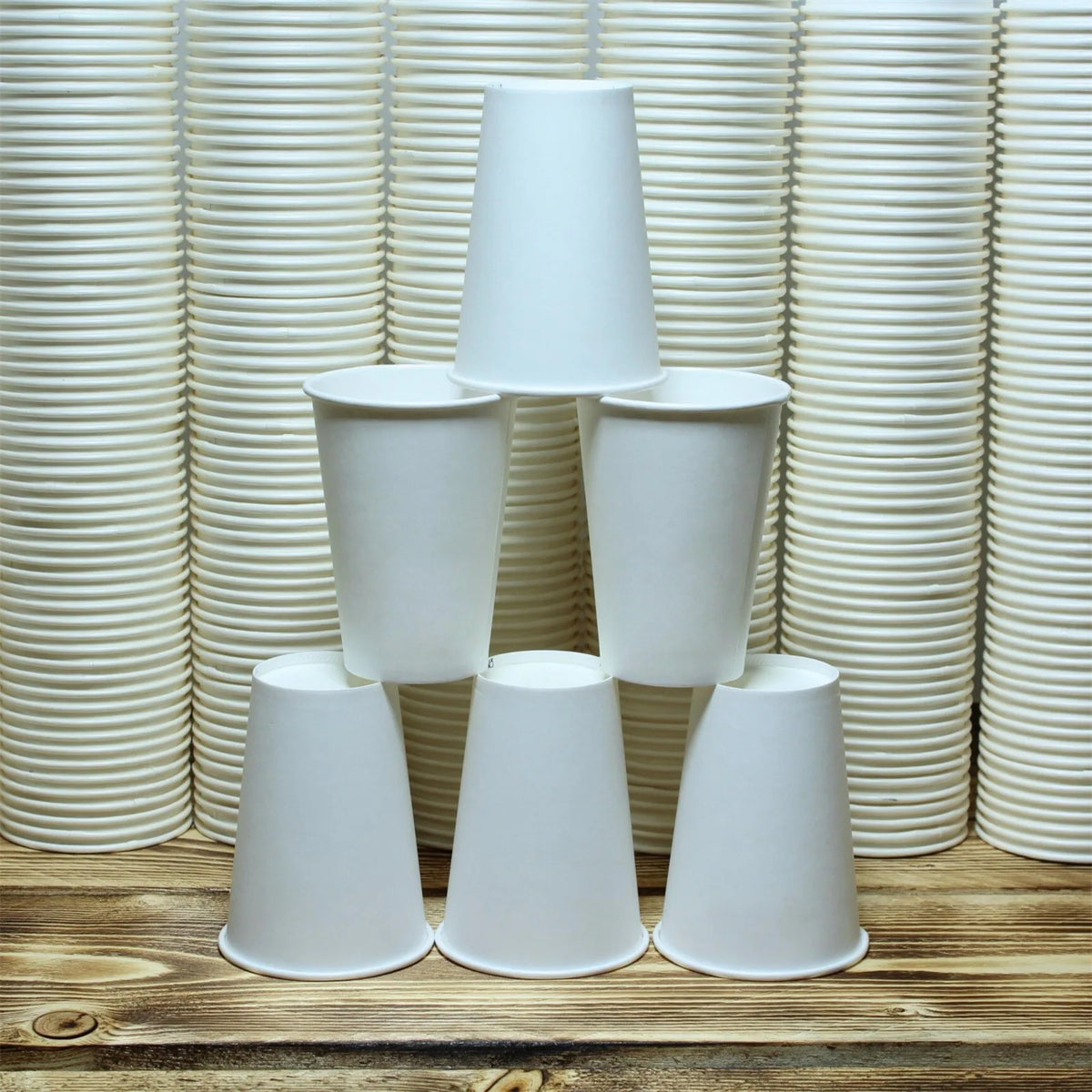 A display of white reusable disposable paper cups arranged in a vertical grid and a row on a wooden surface.