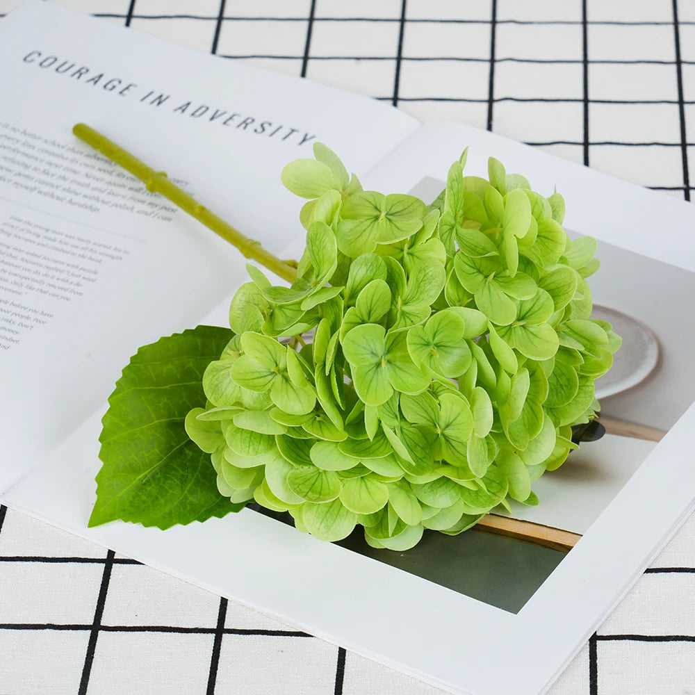 A cluster of bright green artificial hydrangea leaves and stems displayed on a white paper with black grid lines.