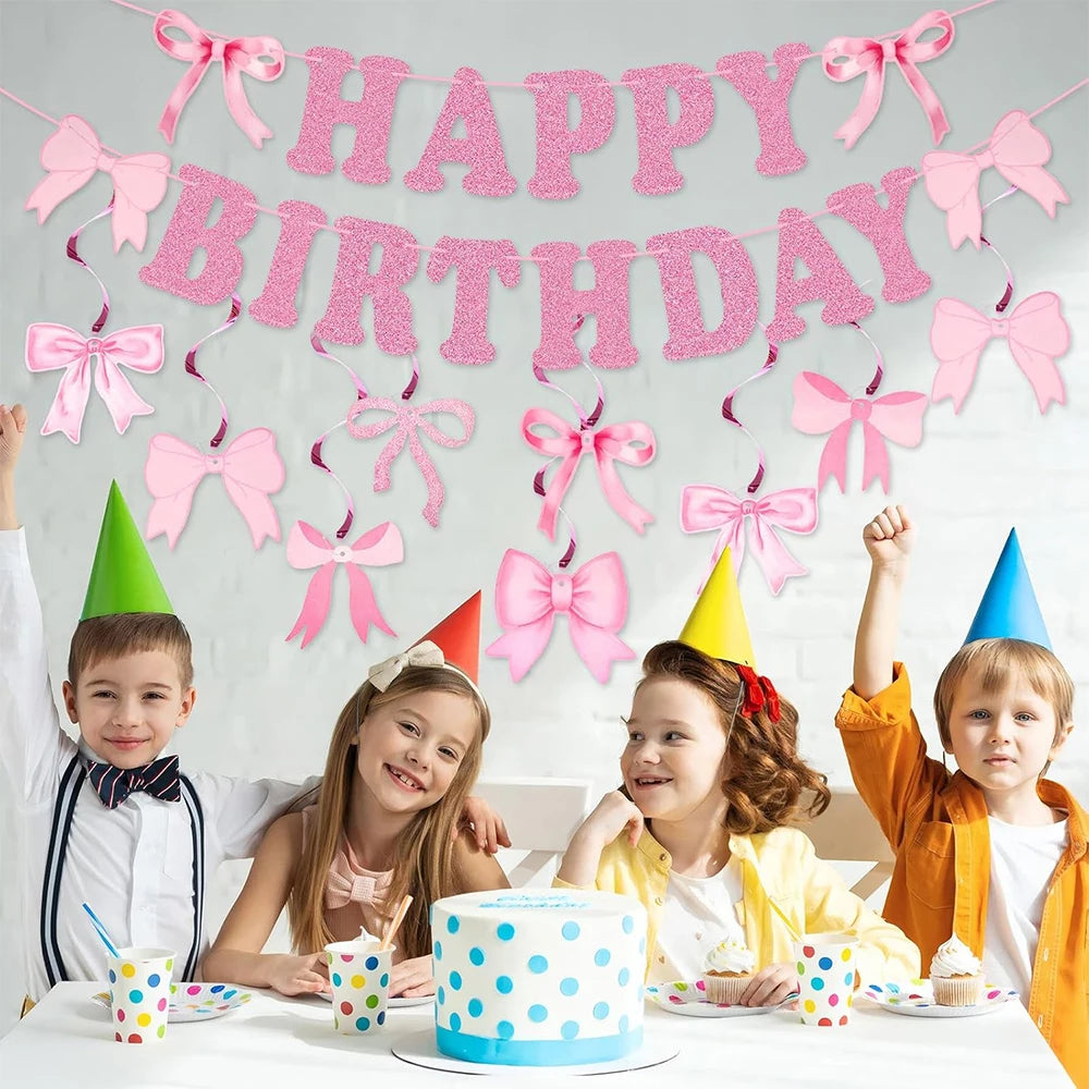 A pink glitter bow birthday banner hangs above a table with children and cupcakes.