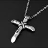 A silver stainless steel cross necklace pendant hanging from a chain against a dark background.