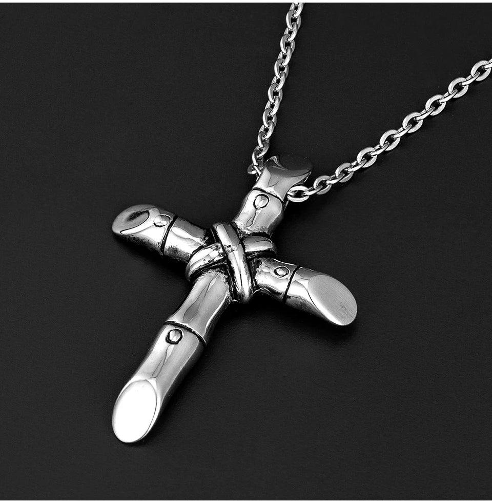 A silver stainless steel cross necklace pendant hanging from a chain against a dark background.