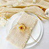 A stack of handcrafted fringed beige cotton napkins resting on white plates with dried floral accents.