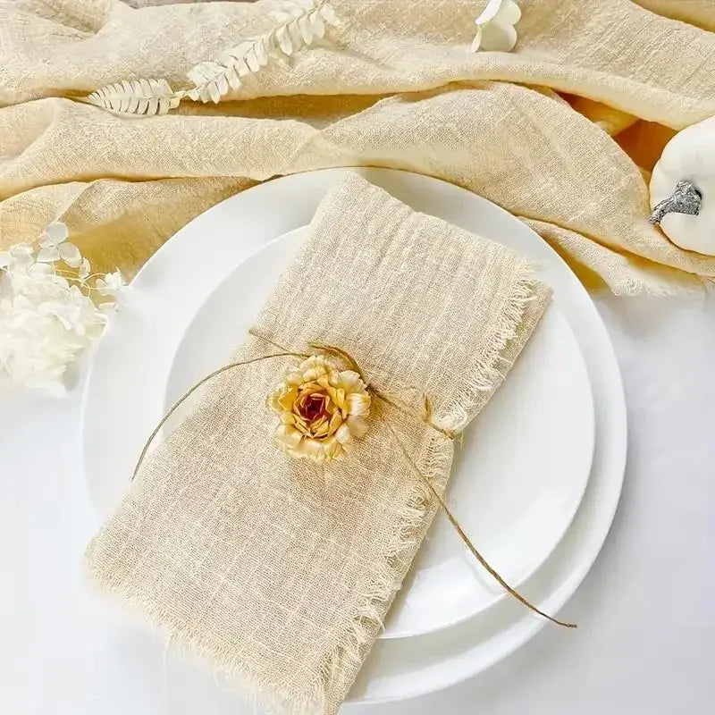A stack of handcrafted fringed beige cotton napkins resting on white plates with dried floral accents.