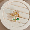 A gold cocktail ring featuring a floral design with clear stones and a green leaf accent, displayed on a light background.
