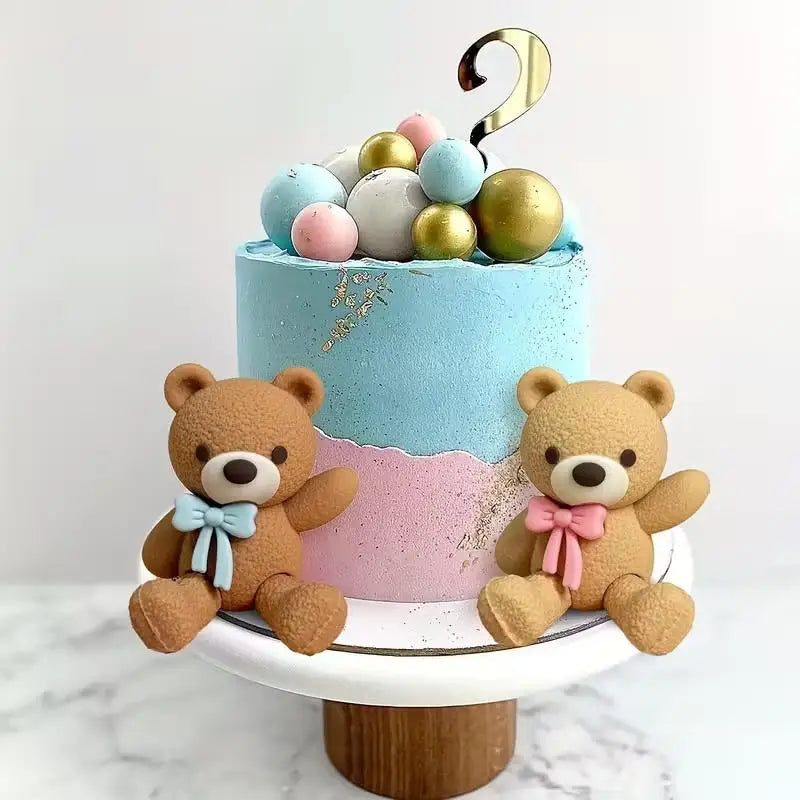 A tiered cake decorated with pastel blue and pink frosting and gold edible toppers, featuring two teddy bears.
