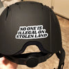 A black helmet with a white sticker that reads No One Is Illegal On Stolen Land