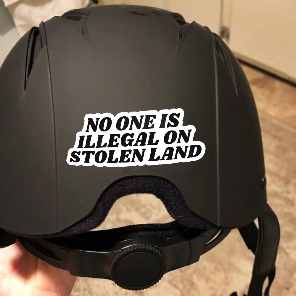 A black helmet with a white sticker that reads No One Is Illegal On Stolen Land