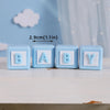 Four light blue baby blocks with the letters B, A, B, and Y are displayed on a white surface.