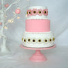 A three-tiered pink and white cake decorated with floral accents displayed on a pink metal stand.