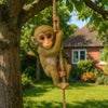 A small monkey figurine is hanging from a tree branch, appearing to climb or dangle.