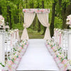 A wedding arch decorated with pink roses and draped fabric, set in a lush green forest.