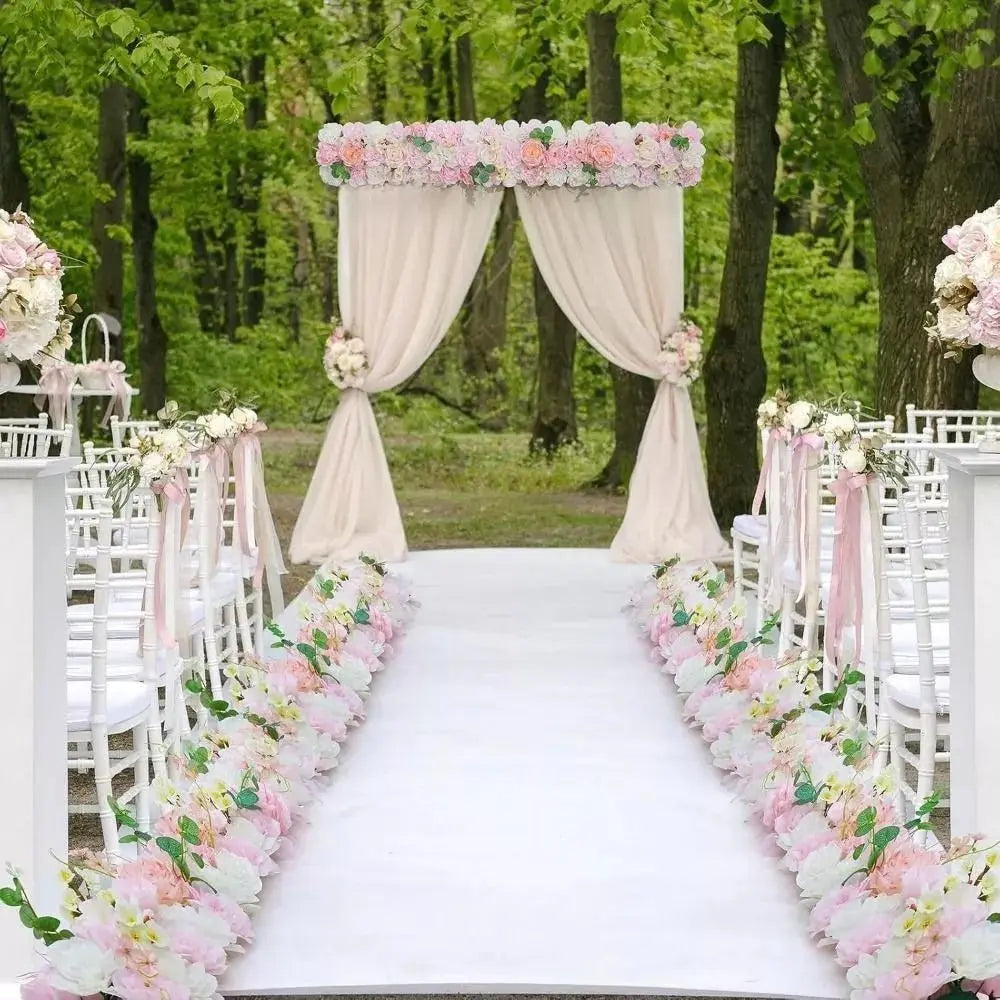 A wedding arch decorated with pink roses and draped fabric, set in a lush green forest.