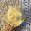 A large, white, squishy cheese cube stress ball is held in a hand against a patterned fabric background.