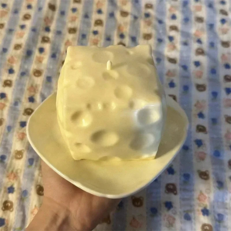 A large, white, squishy cheese cube stress ball is held in a hand against a patterned fabric background.