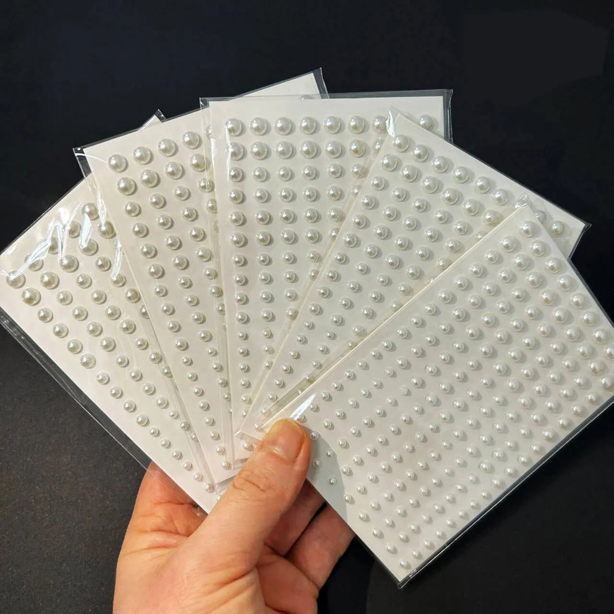 A hand holds several sheets of glitter gem stick-on facial tattoos for cosmetic use.