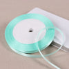 A spool of light mint green satin ribbon lying on a white rectangular box.