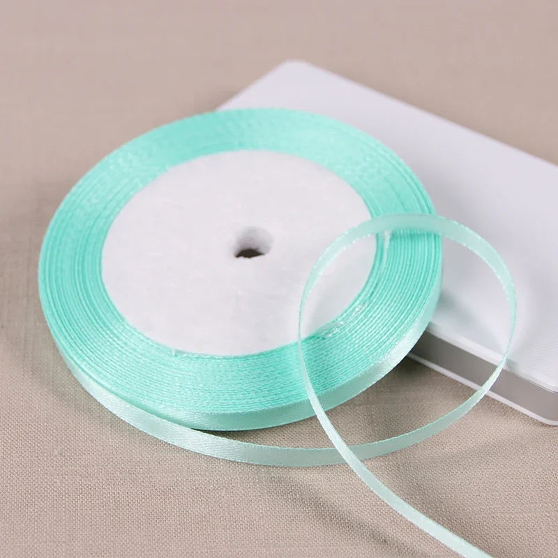 A spool of light mint green satin ribbon lying on a white rectangular box.