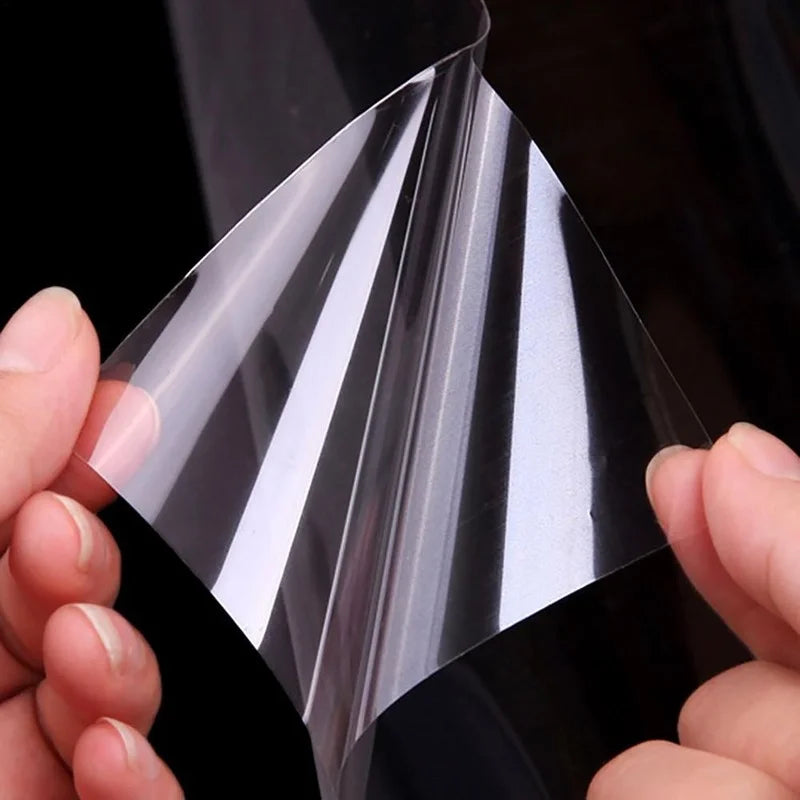 A hand is holding a clear, self-adhesive film that is being peeled back to show its layered structure.