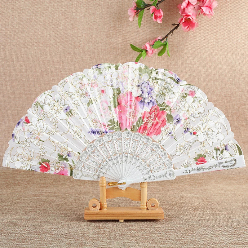 A white silk flower folding fan with pink and purple floral patterns displayed on a wooden stand.